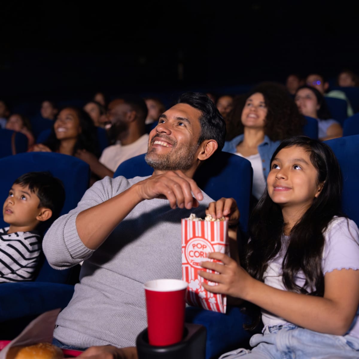 Father and two children watching a movie in a cinema and eating popcorn.