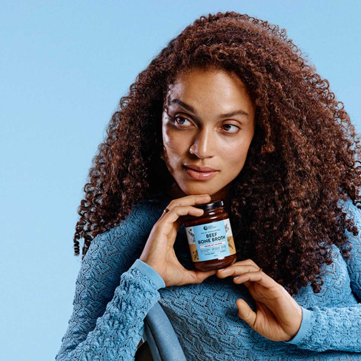 Woman, holding Bone Broth packet on blue background 