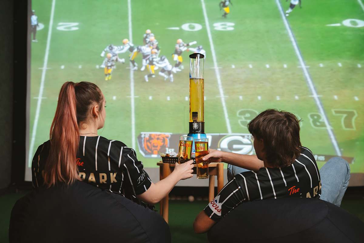 male and female cheersing beers in front of jumbo screen