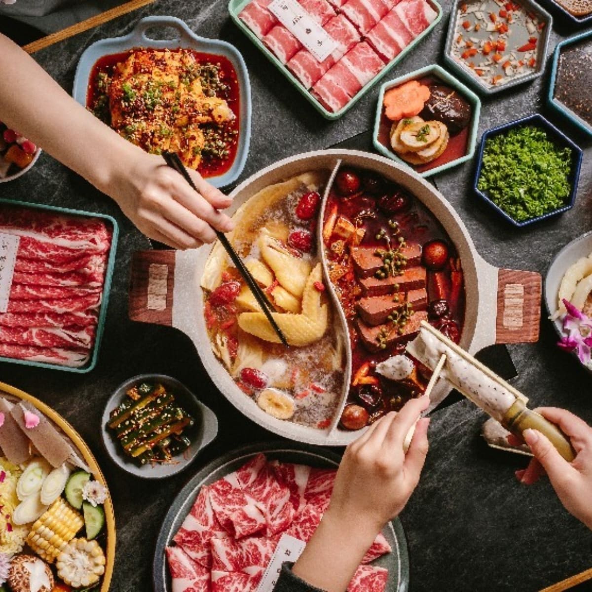 Asian food cooking in a hot pit with peoples hands holding forks to pick up the food