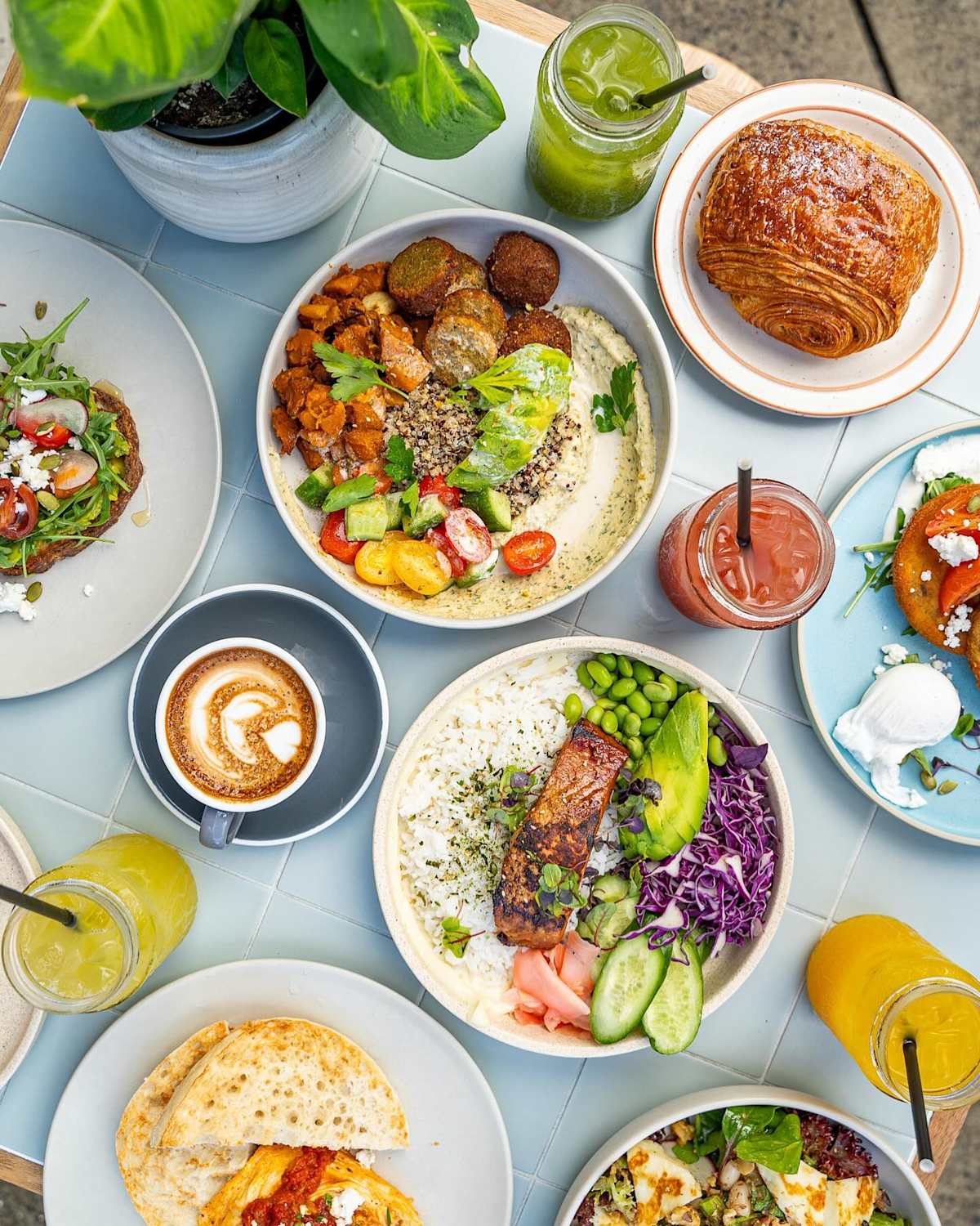 Image of fresh colourful salads, drink and plants on a white tiled table.