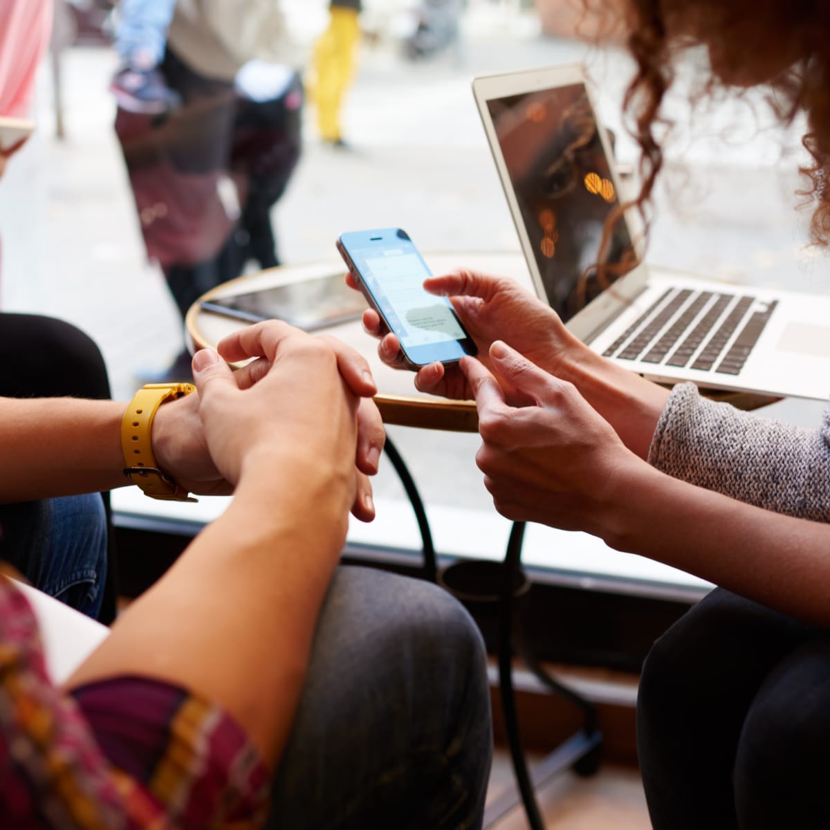 Two people look at a phone at a table with a laptop.
