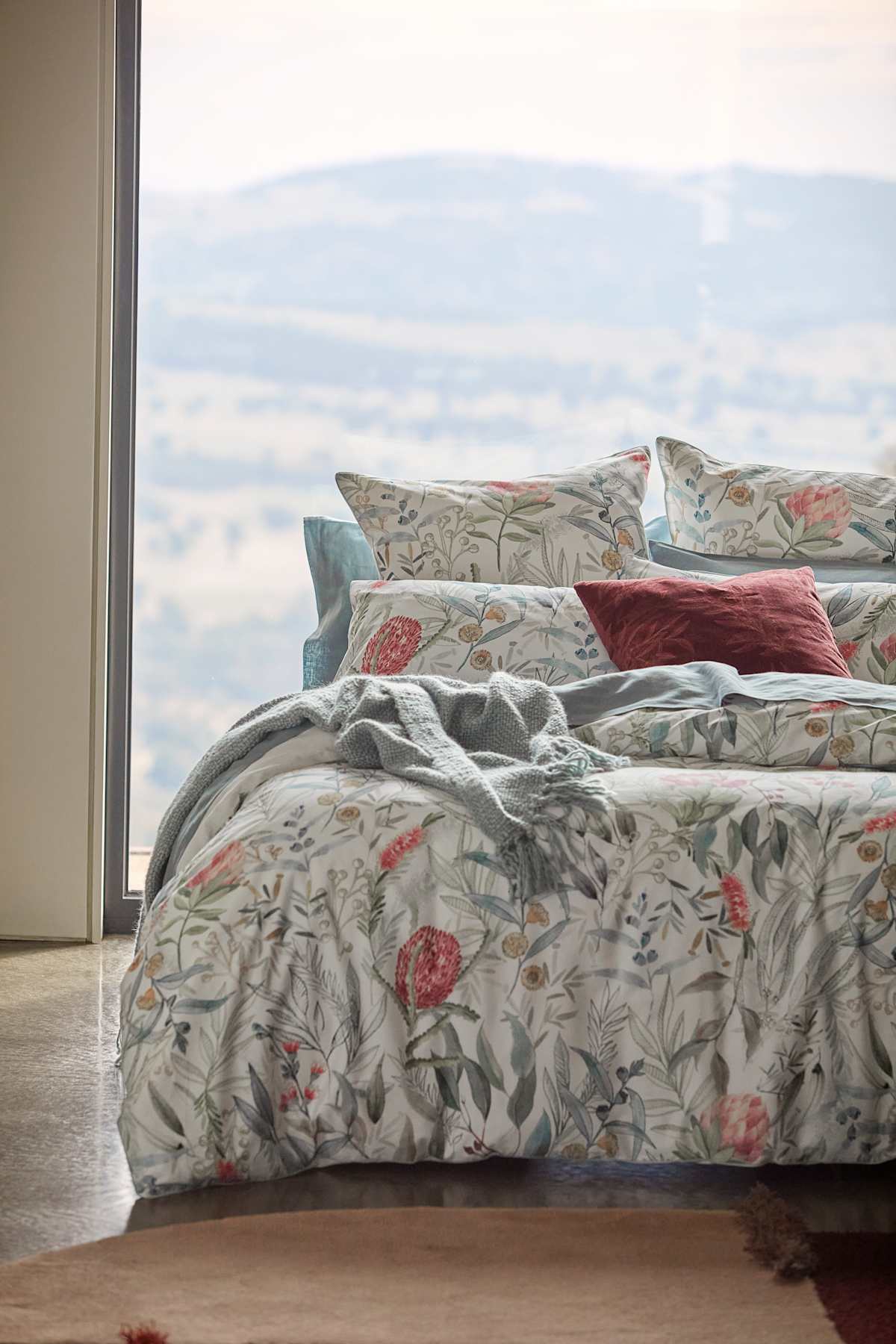 Picture of a bed infront of a large window with mountains in the background.