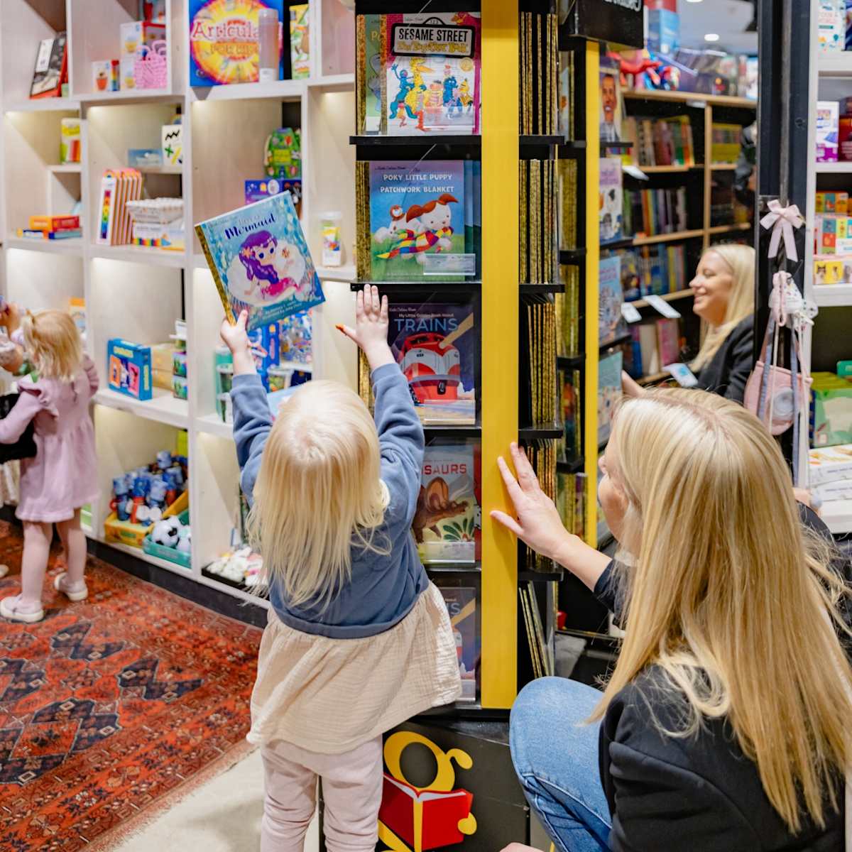 Blonde mother & daughter pick book off bookshelf in Harry Hartog