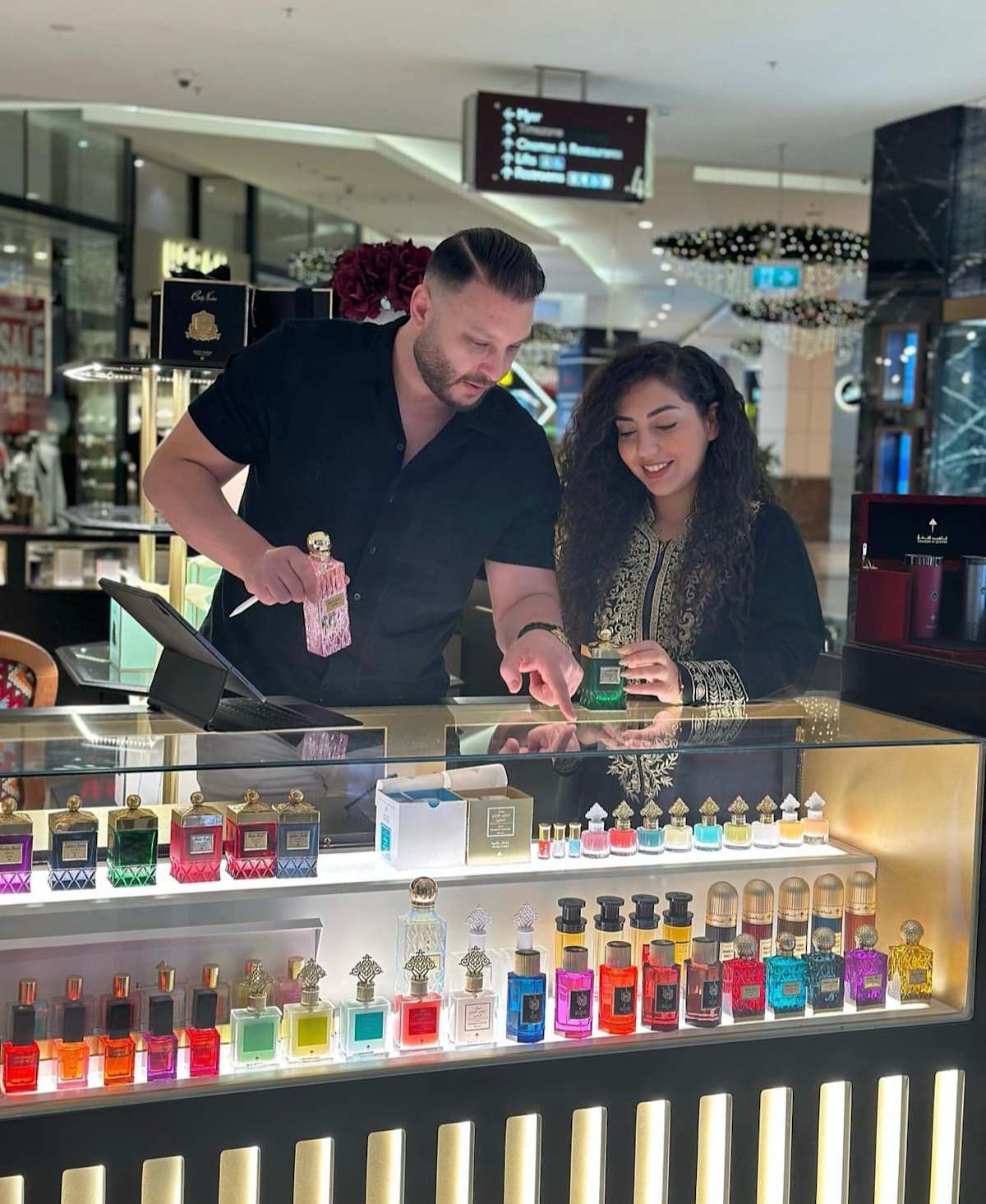 Images of a man and a woman choosing perfume from a glass counter.