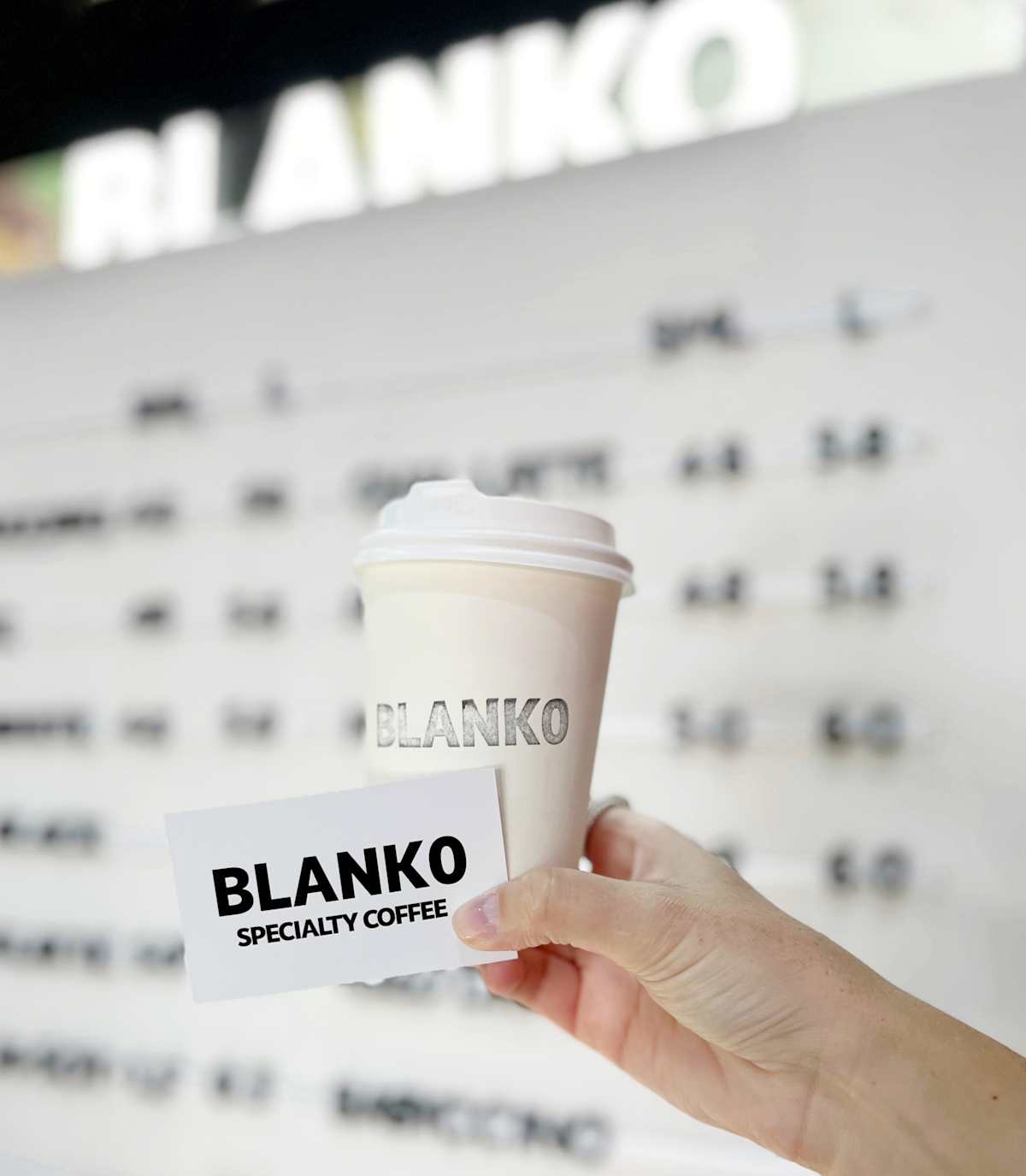 Blanko Specialty Coffee takeaway cup and loyalty card in front of sign