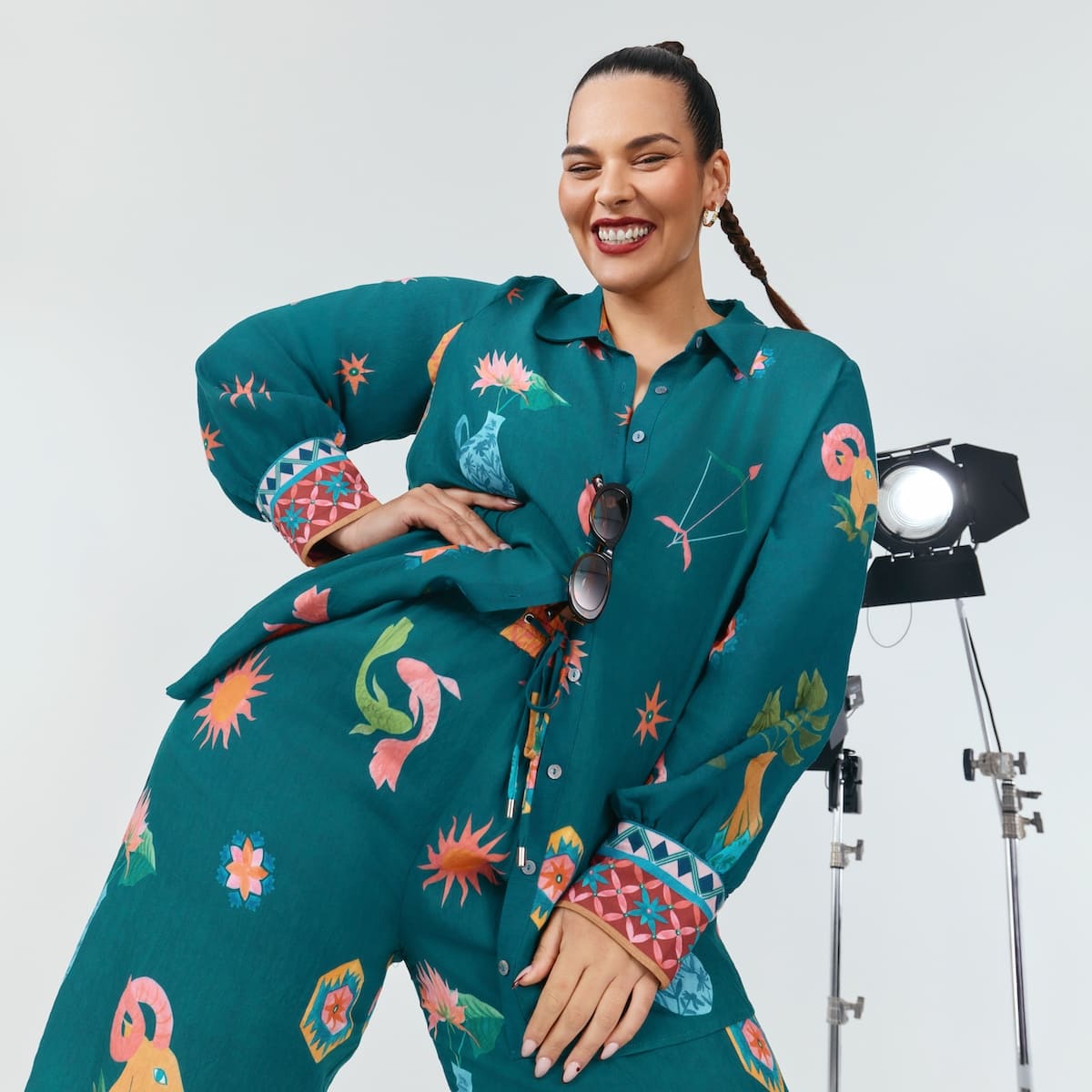 A woman standing withone hand on her hip, wearing a printed green set with button down shirt and pants