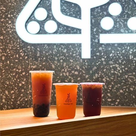 Three Teaology Lab bubble tea cups on a wooden bench.