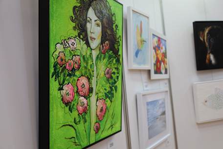 Picture of several artworks hanging on a wall. The feature artwork depicts a lady with brown hair and floral face framing.