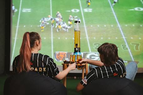 male and female cheersing beers in front of jumbo screen