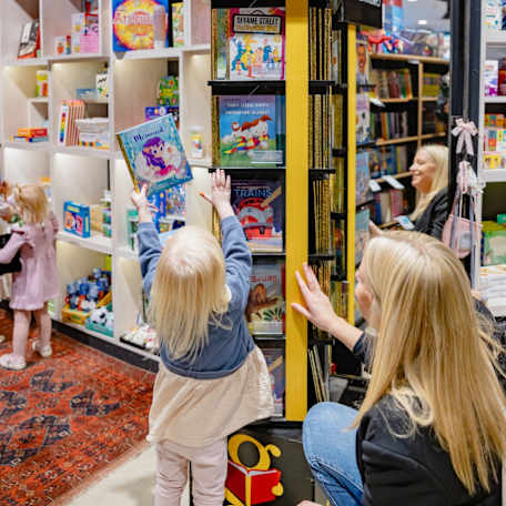 Blonde mother & daughter pick book off bookshelf in Harry Hartog